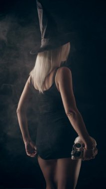 Siyah elbiseli genç sarışın cadı, kafatası tutuyor, Cadılar Bayramı temalı, ağır çekim.