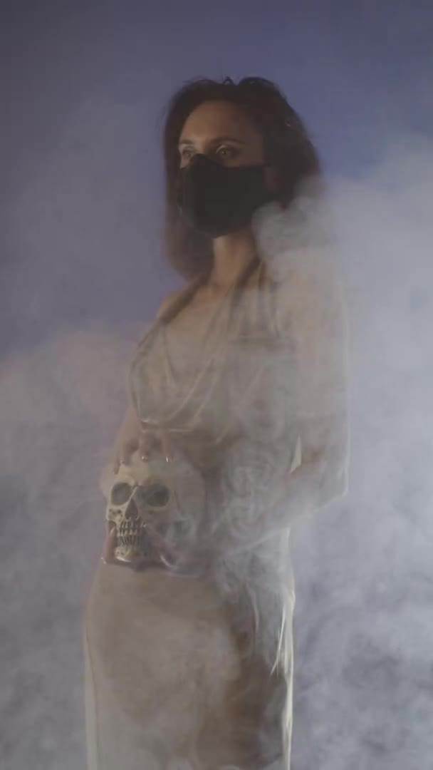 パーティーのドレスを着て 煙の中で頭蓋骨を保持マスク女性 流行概念 垂直ビデオ — ストック動画