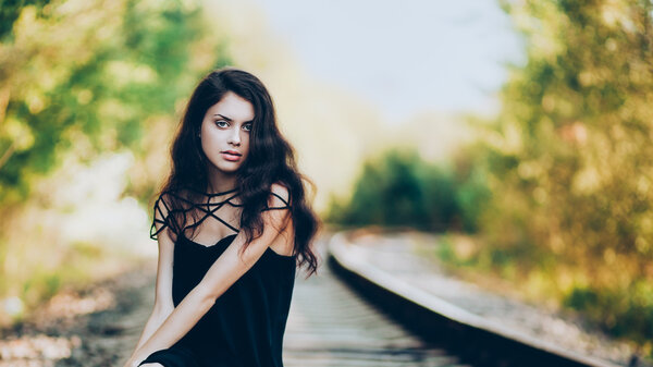 Artistic fashion portrait of young brunette sitting on railroad. Shallow depth of field