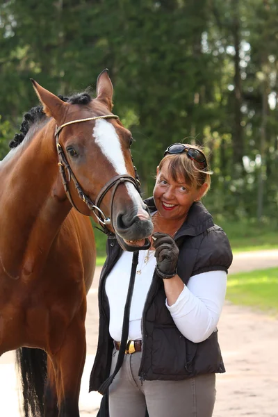 Äldre glad kvinna och brun häst i skogen — Stockfoto