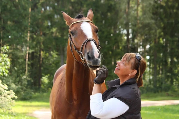 Idosos mulher feliz e cavalo marrom na floresta — Fotografia de Stock