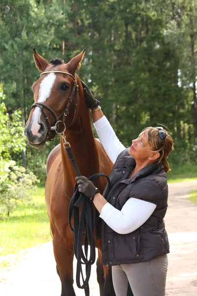 Ältere, glückliche Frau und braunes Pferd im Wald — Stockfoto