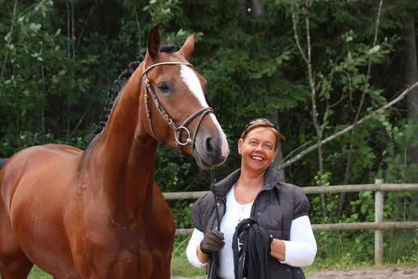 Starší šťastná žena a hnědý kůň v lese — Stock fotografie