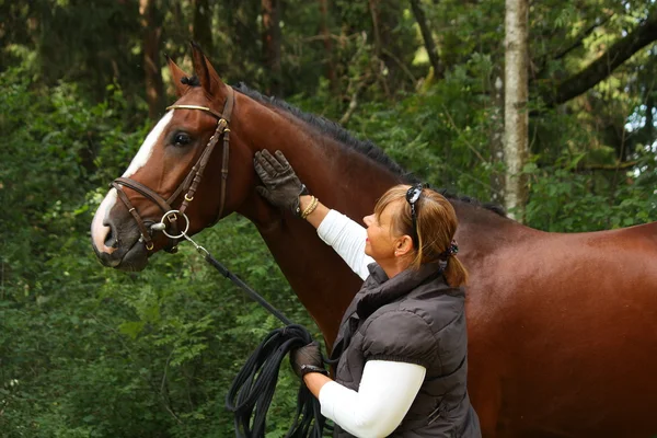 Äldre kvinna och bruna hästen stående i skogen — Stockfoto