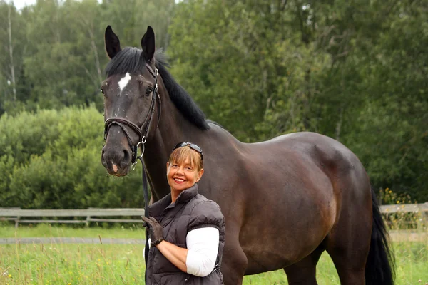 Happy smiling elderly woman and black horse portrait — Stock Photo, Image