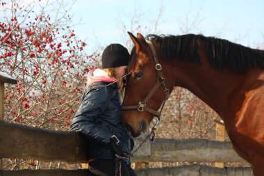 Teenager girl and bay horse hugging each other clipart