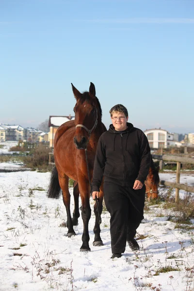 Teenager boy and brown horse walking in the snow — Stock Photo, Image