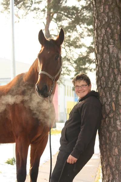 Dospívající chlapec a hnědé koně stojí poblíž stromu — Stock fotografie
