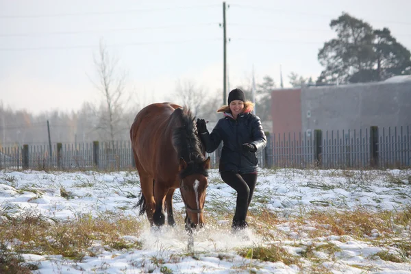 Blond tonåring flicka och brun häst körs i snön — Stockfoto