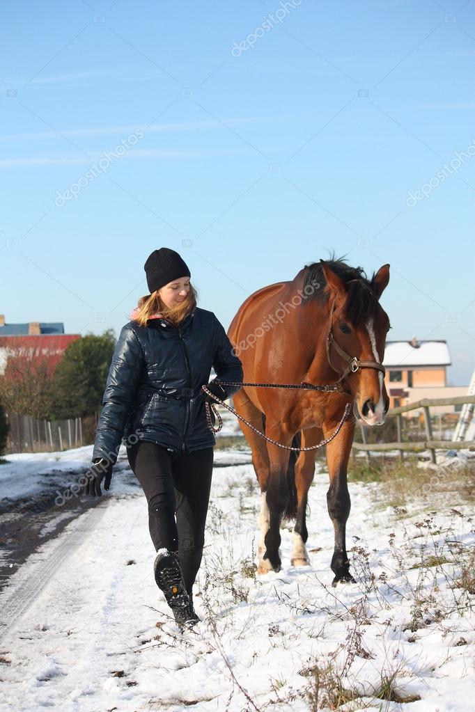 Teenager girl and brown horse walking in the snow