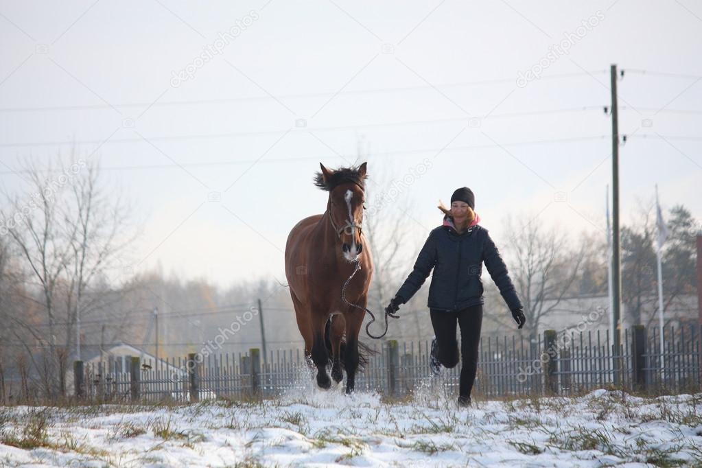 Blonde teenager girl and brown horse running in the snow