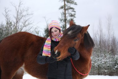 Beautiful teenager girl hugging brown horse in winter clipart