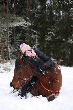 Teenager girl and brown horse lying in the snow clipart