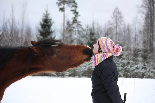 Beautiful teenager girl playfully kissing brown horse in winter — Stock Photo, Image