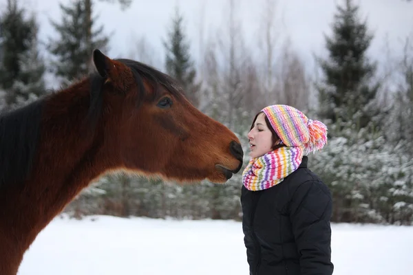 Hermosa adolescente chica juguetonamente besar caballo marrón en invierno — Foto de Stock