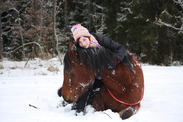 Teenager girl and brown horse lying in the snow — Stock Photo, Image