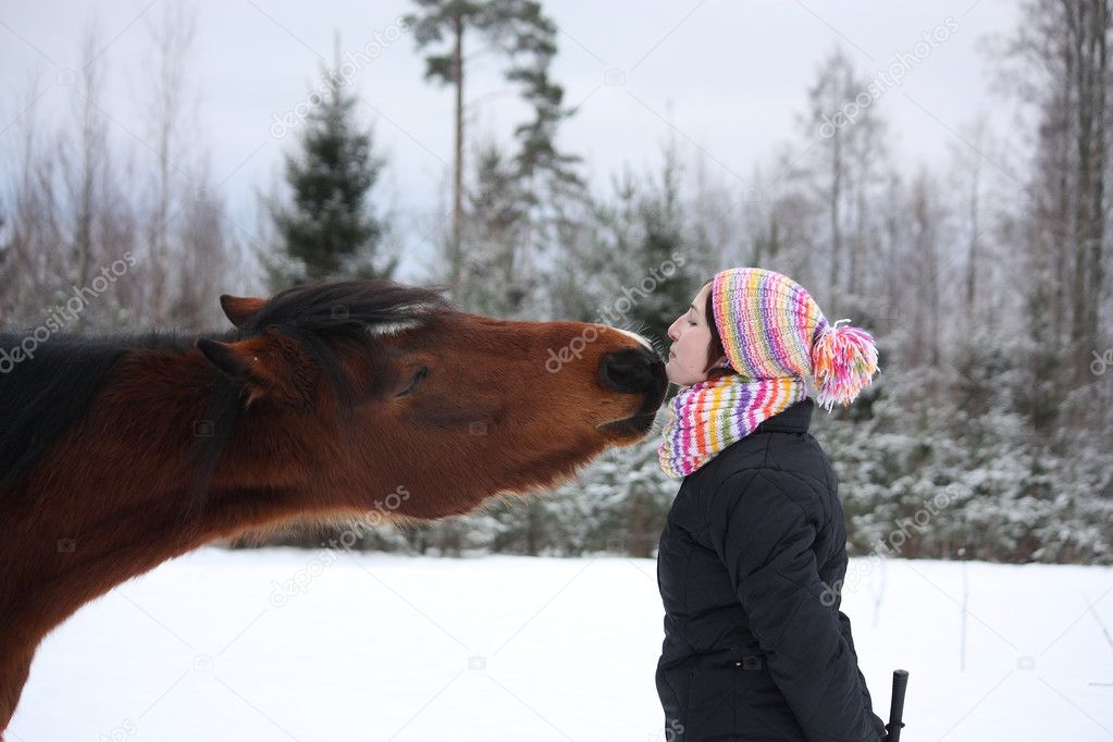 Beautiful teenager girl playfully kissing brown horse in winter