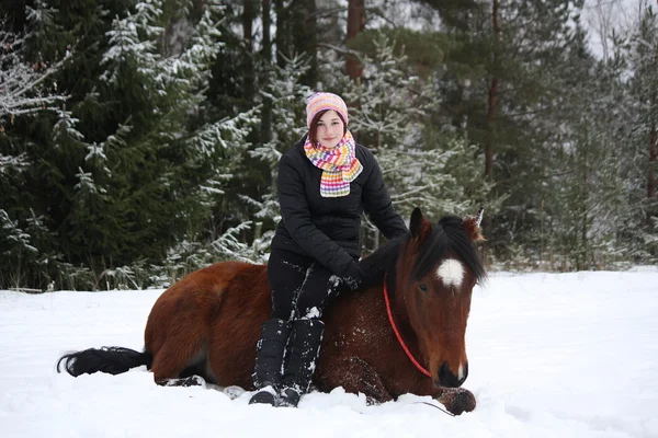 Teenager girl and brown horse lying in the snow — Stock Photo, Image