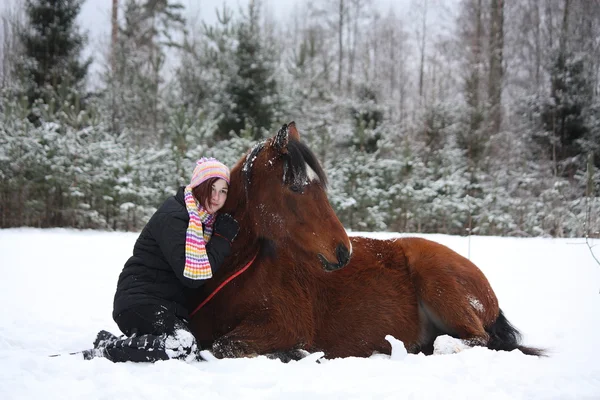 Adolescente et cheval brun couché dans la neige — Photo