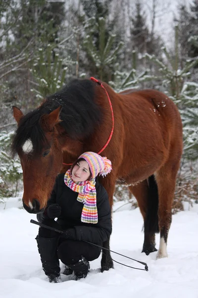 Hermosa chica adolescente sentada cerca de caballo marrón en invierno — Foto de Stock