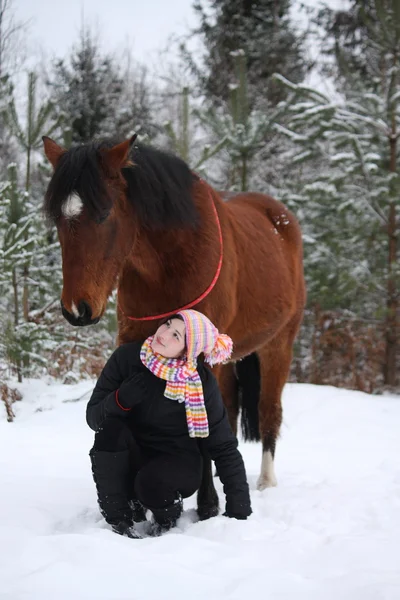 Hermosa chica adolescente sentada cerca de caballo marrón en invierno —  Fotos de Stock