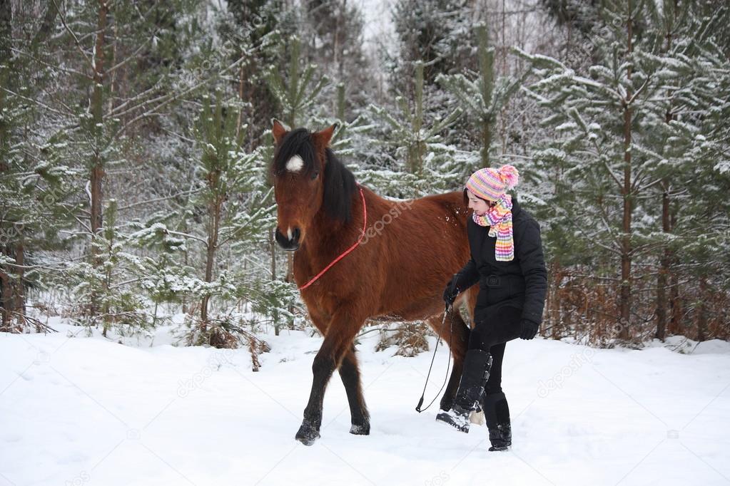 Teenager girl and brown horse walking through the forest togethe