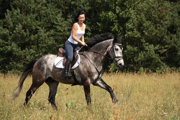 Beautiful woman riding gray horse in the forest