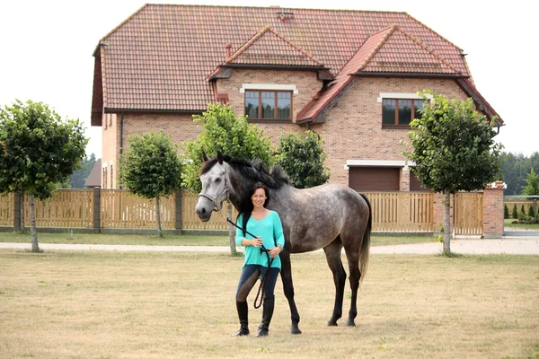Piękna młoda kobieta i koń w pobliżu domku — Zdjęcie stockowe