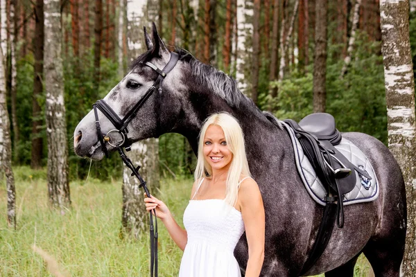 Krásná světlovlasá žena a šedý kůň v lese — Stock fotografie