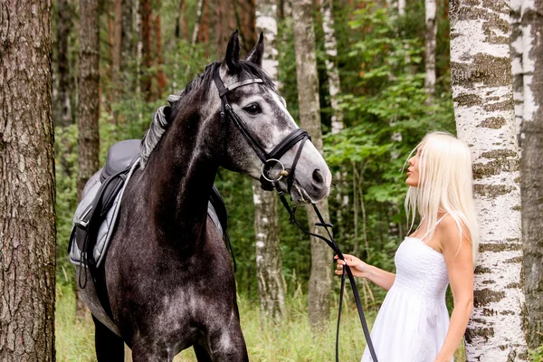 Krásná světlovlasá žena a šedý kůň v lese — Stock fotografie