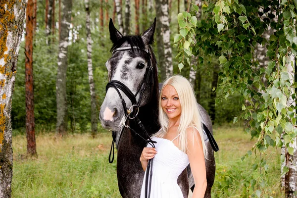 Mulher loira bonita e cavalo cinza na floresta — Fotografia de Stock