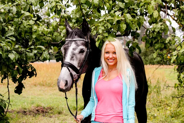 Beautiful blonde woman and her horse in rural area — Stock Photo, Image