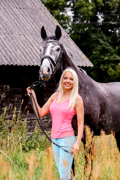 Beautiful blonde woman and her horse in rural area — Stock Photo, Image