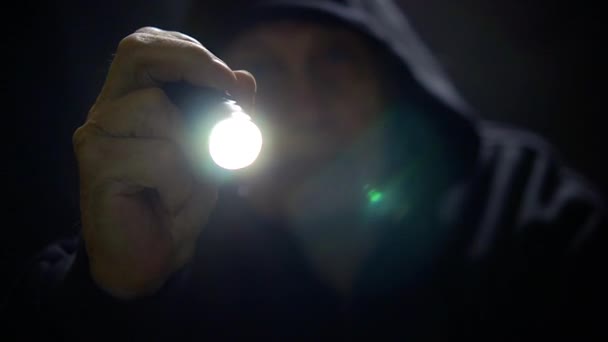 Voleur : dans l'obscurité, la figure d'un homme avec une capuche abaissée, une lampe de poche allumée à la main — Video