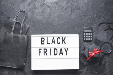 Kara Cuma yazılı pano, alışveriş çantaları, hediyeler ve karanlık arkaplanda hesap makinesi