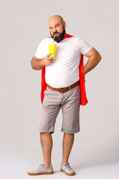 Overweight man in cape and with cola on grey background. Weight loss concept