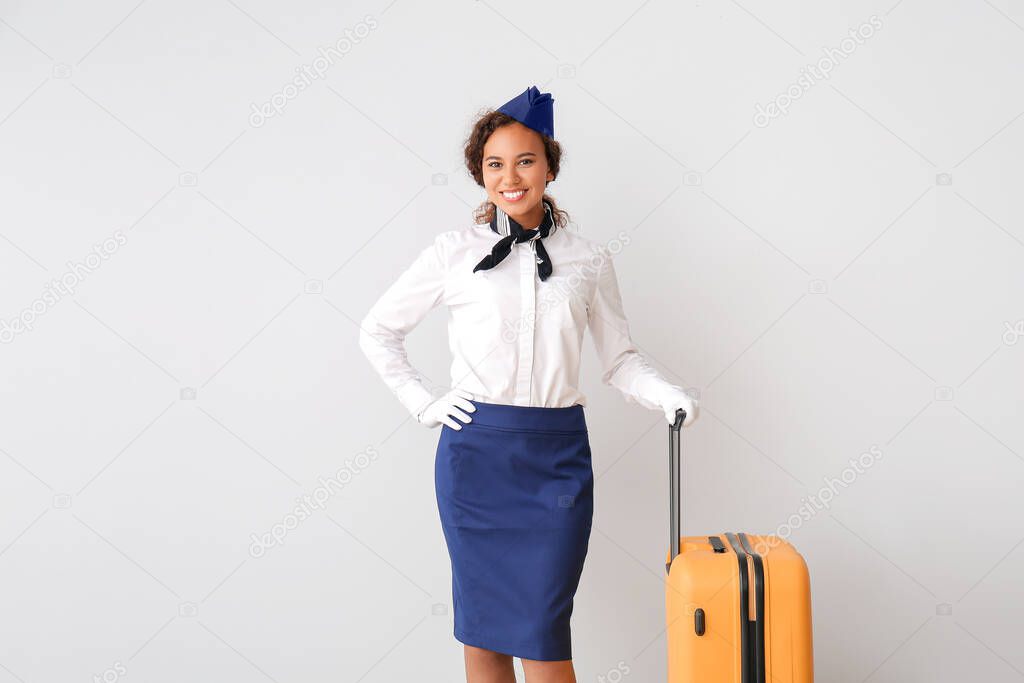 Beautiful African-American stewardess with luggage on grey background
