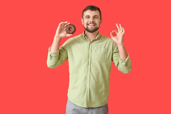 Schöner Junger Mann Mit Süßem Donut Zeigt Auf Farbigem Hintergrund — Stockfoto