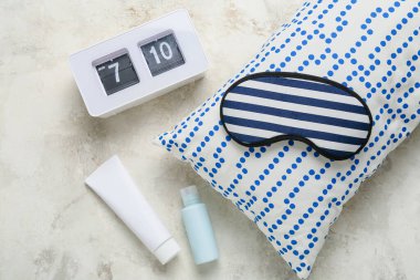 Yastık, uyku maskesi, çalar saat ve arka planda kozmetik ürünler