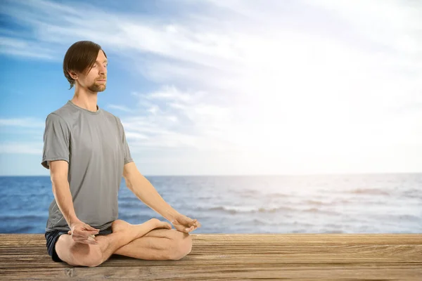 Sporty man practicing yoga near sea