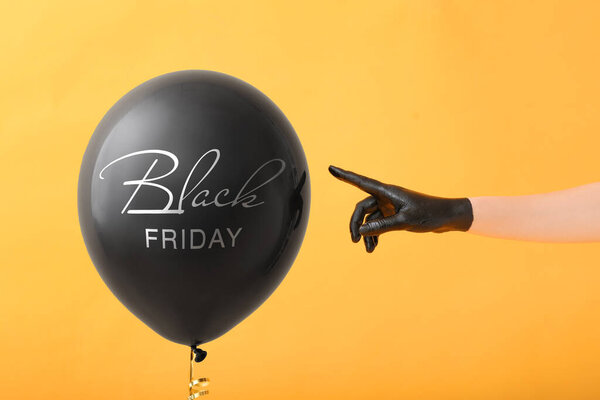 Рука в резиновой перчатке и воздушном шаре с текстом Черная пятница на цветном фоне