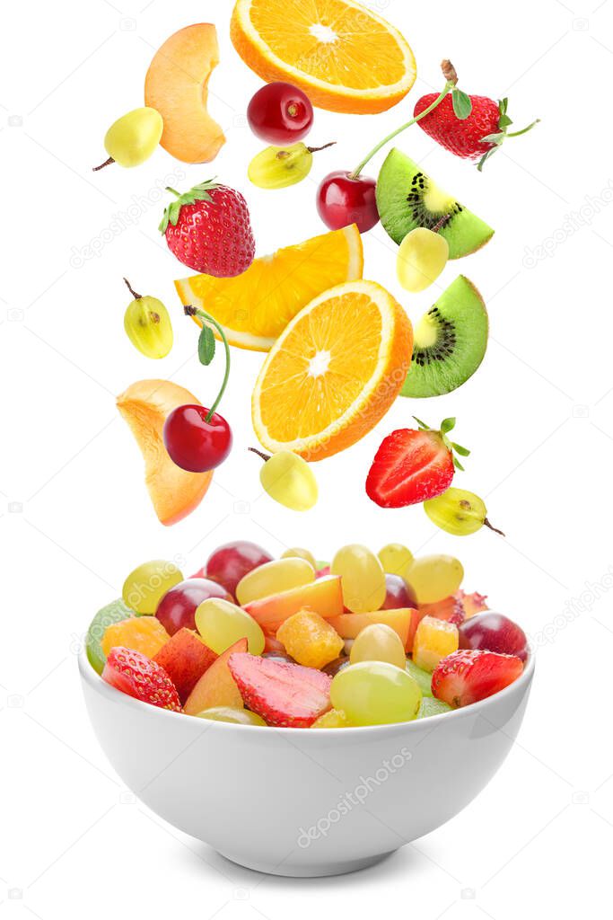 Delicious fruit salad in bowl and flying ingredients on white background
