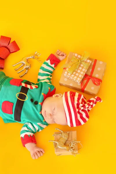 Schlafendes Kleines Baby Elfenkostüm Und Mit Weihnachtsgeschenken Auf Farbigem Hintergrund — Stockfoto