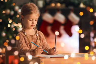 Evde Noel Baba 'ya mektup yazan tatlı küçük bir kız.