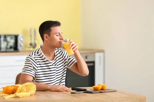 ハンサムな男飲む新鮮なオレンジジュースでキッチン — ストック写真