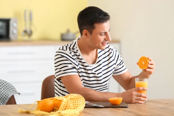 ハンサムな男絞る新鮮なオレンジジュースでキッチン — ストック写真