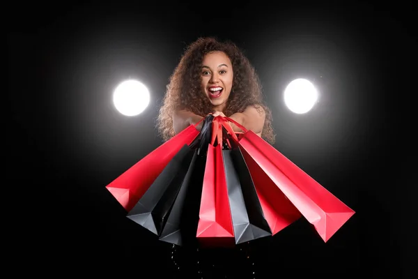 暗い背景にショッピングバッグと幸せなアフリカ系アメリカ人女性 ブラック フライデー販売 — ストック写真