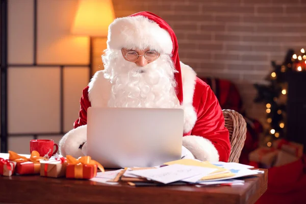 Santa Claus with laptop checking e-mail at home on Christmas eve