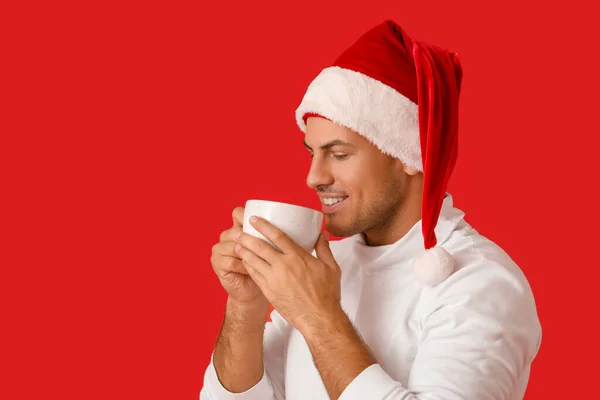 Schöner Junger Mann Mit Weihnachtsmütze Und Heißem Tee Auf Farbigem — Stockfoto