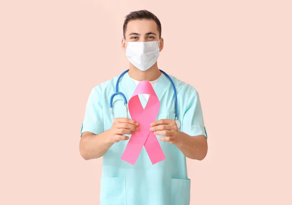 Doctor with pink ribbon on color background. Breast cancer awareness concept